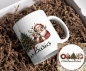 Preview: Ein weißer Keramikbecher, verpackt in einer Geschenkbox, liegt auf einer Unterlage aus braunem Papierfüllmaterial. Auf dem Becher ist eine festliche Illustration abgebildet: Ein fröhlich dreinblickender Weihnachtsmann, der ein Rentier liebevoll umarmt. Ne
